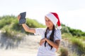 Portrait of a pretty smiling teenage girl in a red Santa hat and making selfie on a sand tropical beach Royalty Free Stock Photo
