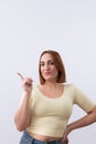 Portrait of a pretty smiling woman dressed in casual clothes pointing her finger to the side on light background. Royalty Free Stock Photo