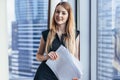 Portrait of pretty smiling young woman holding papers standing at window with cityscape view Royalty Free Stock Photo