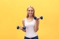 Portrait of pretty sporty girl holding weights and smiling. Isolated over yellow background. Royalty Free Stock Photo