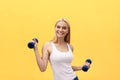 Portrait of pretty sporty girl holding weights and smiling. Isolated over yellow background. Royalty Free Stock Photo