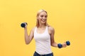 Portrait of pretty sporty girl holding weights and smiling. Isolated over yellow background. Royalty Free Stock Photo