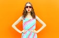 Portrait pretty woman blowing red lips sends sweet air kiss wearing red heart shaped sunglasses, colorful striped dress on orange Royalty Free Stock Photo