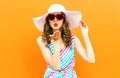 Portrait pretty woman blowing red lips sends sweet air kiss wearing summer straw hat, colorful striped dress on orange wall Royalty Free Stock Photo