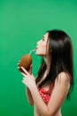 Portrait of Pretty Woman with Long Dark Hair in Bright Swimsuit Drinking Tropical Cocktail on Green Background in Studio Royalty Free Stock Photo