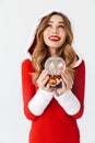 Portrait of pretty woman 20s wearing Santa Claus red costume smiling and holding Christmas snow ball, isolated over white Royalty Free Stock Photo
