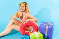 Portrait of pretty woman in swimsuit sitting with rubber ring and many gift boxes, drinking fresh juice or cocktail Royalty Free Stock Photo