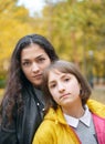 Portrait of pretty woman and teen girl. They are posing in autumn park. Beautiful landscape at fall season Royalty Free Stock Photo