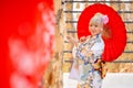 Portrait of pretty woman wear japanese style dress and hold red umbrella during attractive on wood banner in front of row of Royalty Free Stock Photo