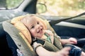 Portrait of pretty 1 year old toddler boy sitting in car safety seat mounted in the front seat. Child transportation safety