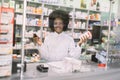 Portrait of pretty young African pharmacist behind the glass, smiling at camera in modern drugstore at the counter Royalty Free Stock Photo