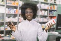 Portrait of pretty young African pharmacist with medications in her hands, smiling at camera in modern drugstore Royalty Free Stock Photo