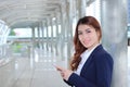 Portrait of pretty young Asian business woman holding mobile smart phone and looking on camera at walkway with copy space backgrou Royalty Free Stock Photo