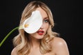 Young blonde woman with bright makeup red lips posing isolated over black wall background holding white flower Royalty Free Stock Photo