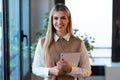 Pretty young businesswoman looking at camera while holding digital tablet standing in the office Royalty Free Stock Photo