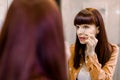 Portrait of pretty young Caucasian woman looking in mirror in bathroom, while cleaning her eye with a cotton swab. Skin Royalty Free Stock Photo