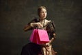 Portrait of pretty, young, elegant girl, royal person in vintage dress holding many shopping bags against dark green