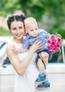 Portrait of pretty young female bride walking, holding baby boy with wedding roses bouquet and looking into camera at sunny summer Royalty Free Stock Photo