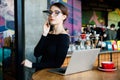 Portrait of pretty young freelancer woman on coffee shop. Beautiful lady with smart phone in her hands using laptop and looking at Royalty Free Stock Photo