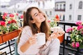 Portrait pretty young girl with long hair having breakfast on balcony in the morning. She holds a cup, croissant, keeps