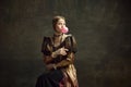 Portrait of pretty young girl, medieval princess in vintage dress posing with bubble gum against dark green background.