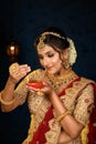 Portrait of a pretty young Indian woman dressed in traditional lehenga, gold jewellery and bangles holding diya in hands on