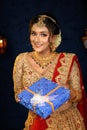 Portrait of a pretty young Indian woman dressed in traditional lehenga, gold jewellery and bangles holding gift box in hands on Royalty Free Stock Photo