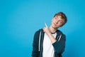 Portrait of pretty young man in casual clothes pointing index fingers aside and looking up isolated on blue wall Royalty Free Stock Photo