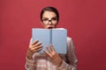 Portrait of a pretty young surprised woman hiding behind an open book and looking away on red background Royalty Free Stock Photo