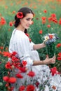 Portrait of a pretty young woman on the background of a blooming poppy field. Ukrainian woman sitting with a bouquet of Royalty Free Stock Photo