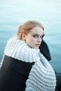 Pretty young woman with blonde hair wearing white woolen scarf sitting on wooden pier