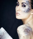 Portrait of pretty young woman with creative make up like snake, fashion victim python skin clutch