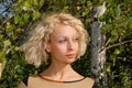 A portrait of a pretty young woman with a curly, blond hair and blue eyes, standing near a birch and looking into the left side. Royalty Free Stock Photo