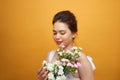 Portrait of a pretty young woman holding bouquet of carnation over yellow background