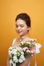 Portrait of a pretty young woman holding bouquet of carnation over yellow background