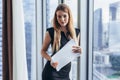 Portrait of pretty young woman holding documents looking at camera standing in office Royalty Free Stock Photo