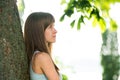 Portrait of pretty young woman with long hair standing neat tree trunk in summer