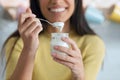 Pretty young woman looking at camera while eating yogurt sitting on the kitchen at home Royalty Free Stock Photo