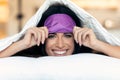 Pretty young woman pulling up sleeping mask while looking at camera after wake up in the bedroom at home Royalty Free Stock Photo