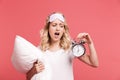 Portrait of pretty young woman 20s wearing sleeping mask holding alarm clock and pillow Royalty Free Stock Photo