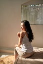 Portrait of pretty young woman sitting on bed applying body cream at home Royalty Free Stock Photo