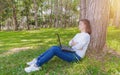 Portrait of pretty young woman sitting on green grass in park summer day while using laptop Royalty Free Stock Photo