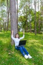 Portrait of pretty young woman sitting on green grass in park summer day while using laptop Royalty Free Stock Photo