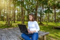 Portrait of pretty young woman sitting on wooden chair in park with legs crossed during summer day while using laptop Royalty Free Stock Photo
