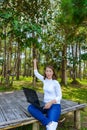 Portrait of pretty young woman sitting on wooden chair and Success gesture in park with legs crossed during summer day while using Royalty Free Stock Photo