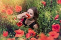 Portrait of a pretty young woman in sportswear sitting in blooming poppies field Royalty Free Stock Photo