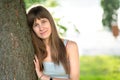 Portrait of pretty young woman standing neat tree trunk in summer