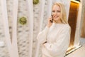 Portrait of pretty young woman talking using mobile phone standing in hotel lounge, looking at camera. Smiling blonde Royalty Free Stock Photo