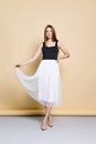 Portrait of pretty young woman in tank top lifting hem of white skirt