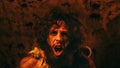 Portrait of Primeval Caveman Wearing Animal Skin Standing in His Cave At Night, Holding Torch with